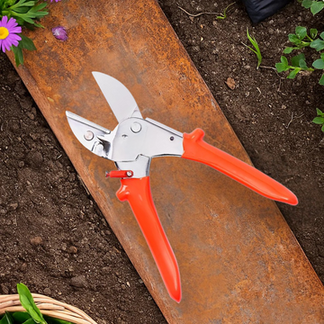 Gardening shears with orange handles on a rusty metal surface near soil and plants.
